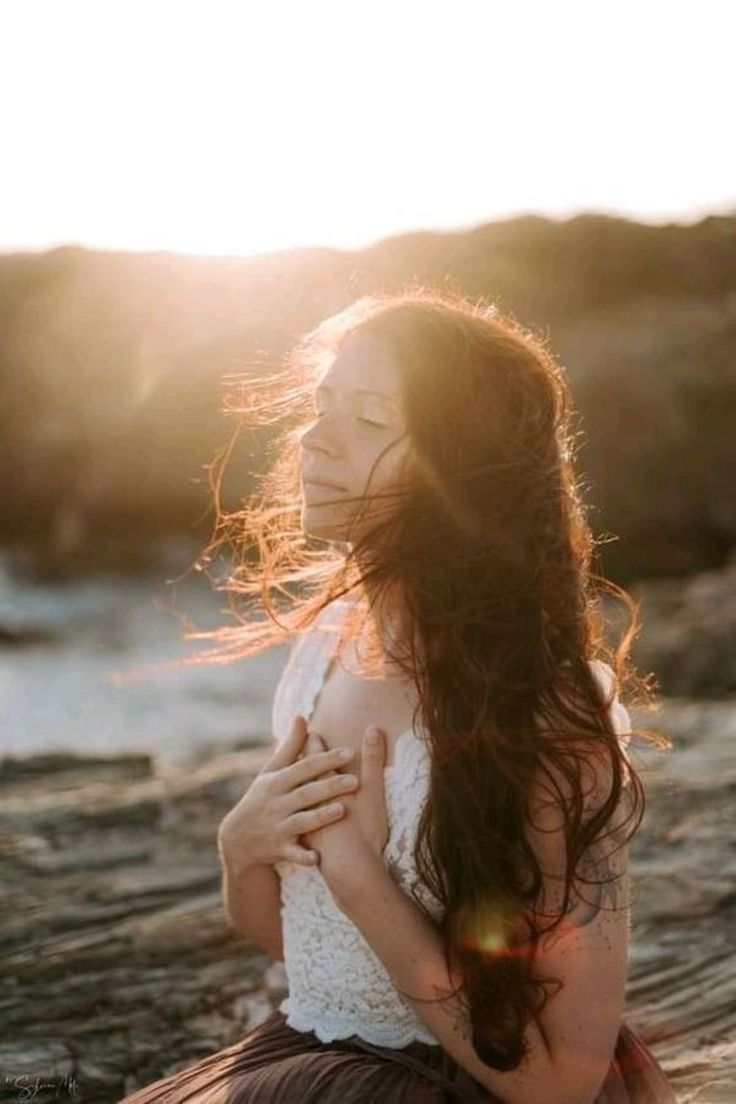 Mujer en la playa con el cabello movido por el viento al atardecer