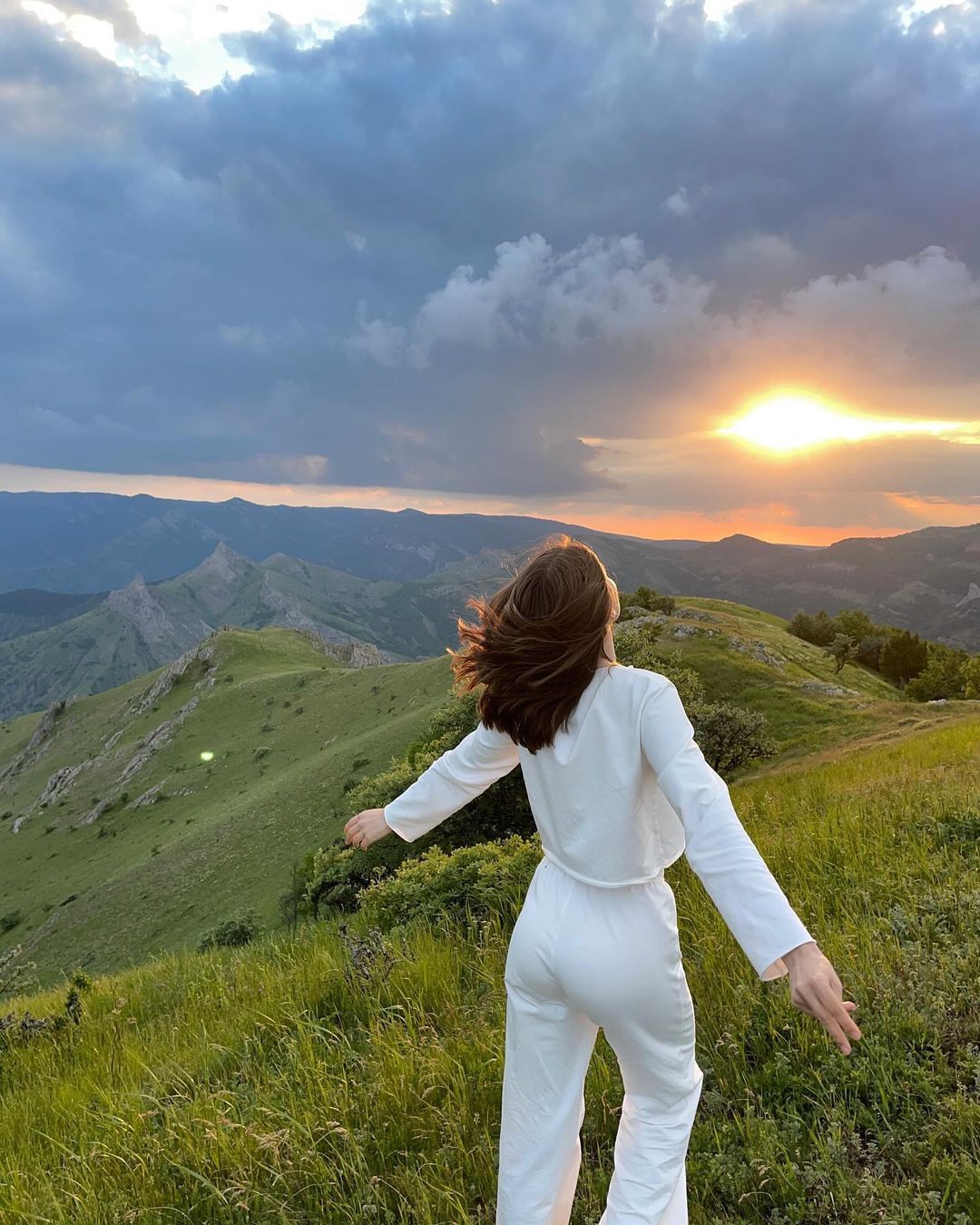 Mujer con brazos abiertos frente a un paisaje de montaña al atardecer